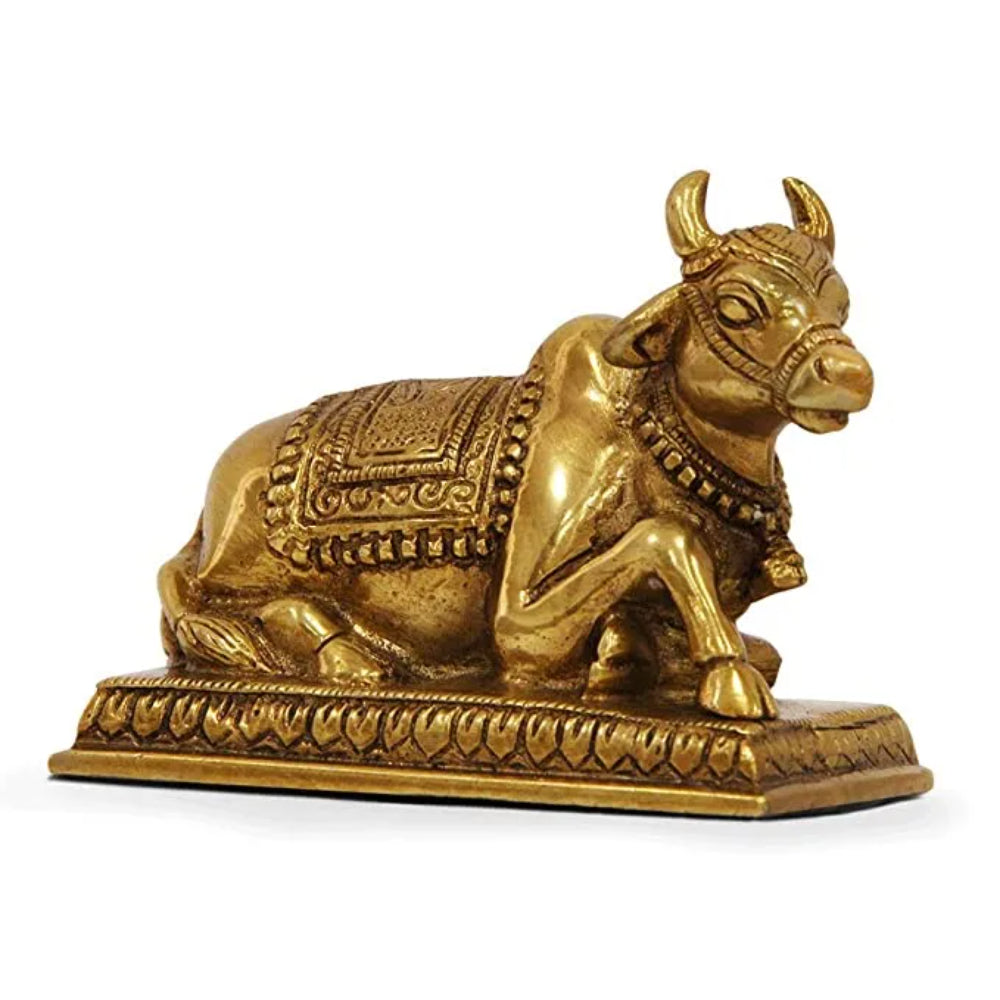 Brass statue of Nandi, the sacred bull, depicted in a seated position with intricate carvings and patterns, adorned with a decorative blanket and necklace, resting on an ornately decorated base.