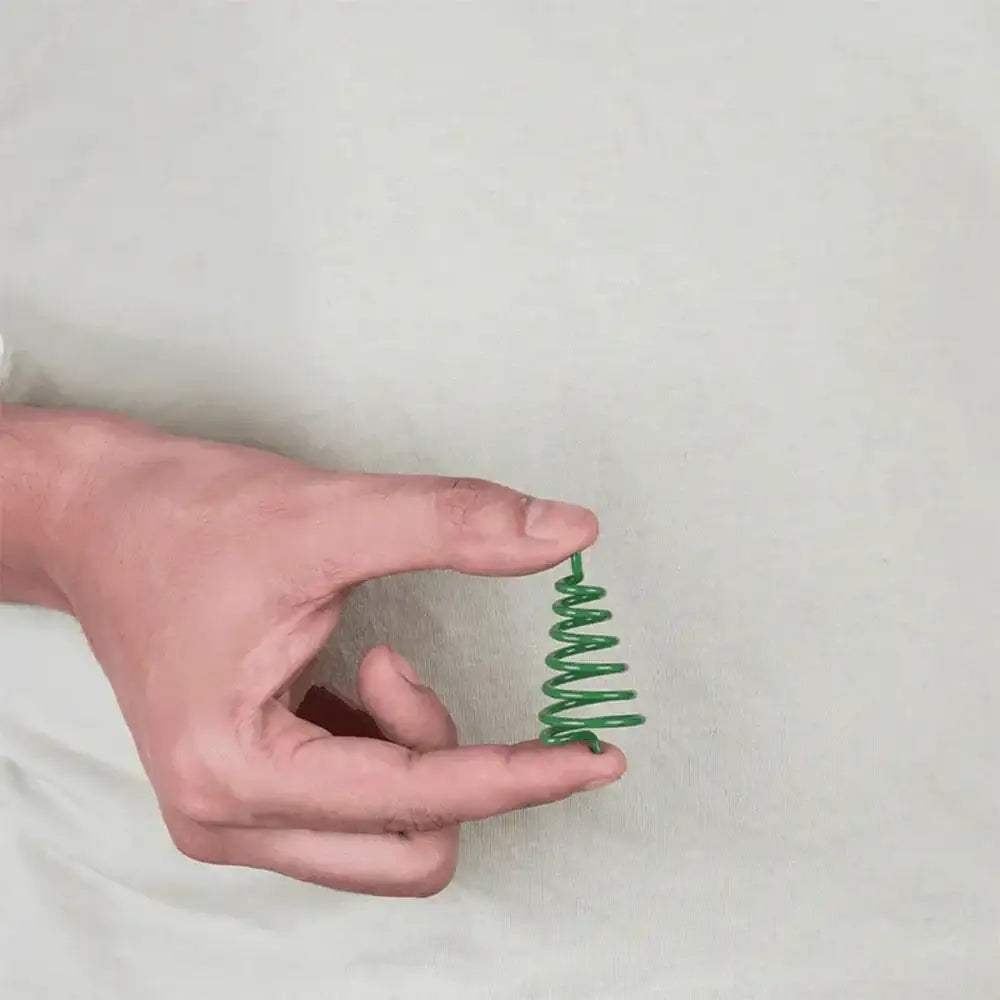 A hand holding a small green spiral spring against a neutral background.