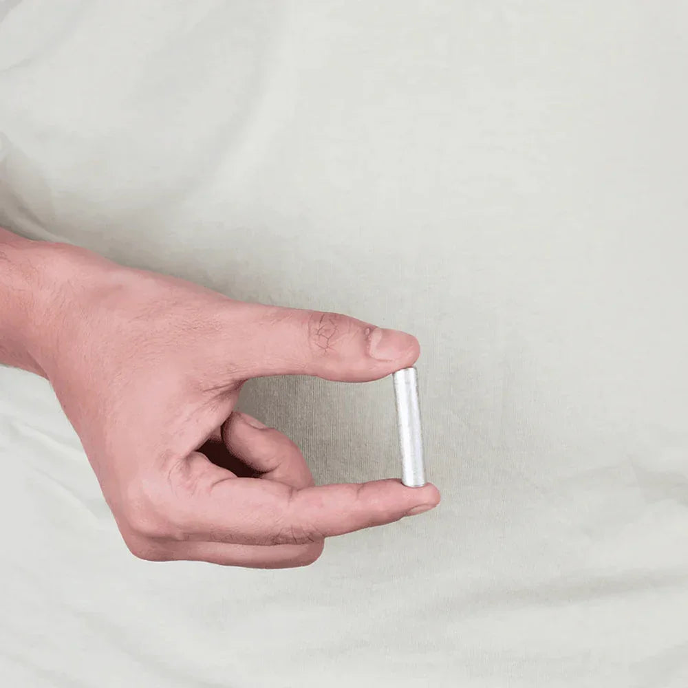 Hand holding a small cylindrical aluminium Vastu remedy metal strip against a plain background