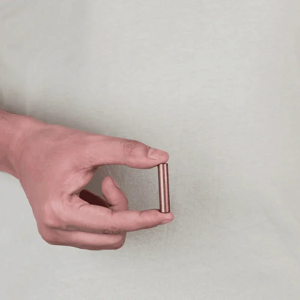 Hand holding a copper metal strip MahaVastu remedy against a plain background