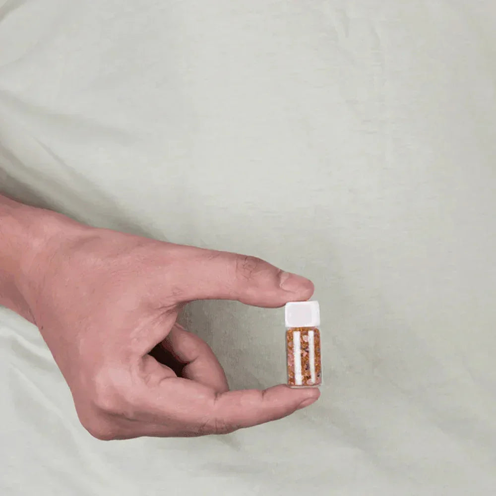 Hand holding a small bottle of MahaVastu Gomed remedy crystals against a light background