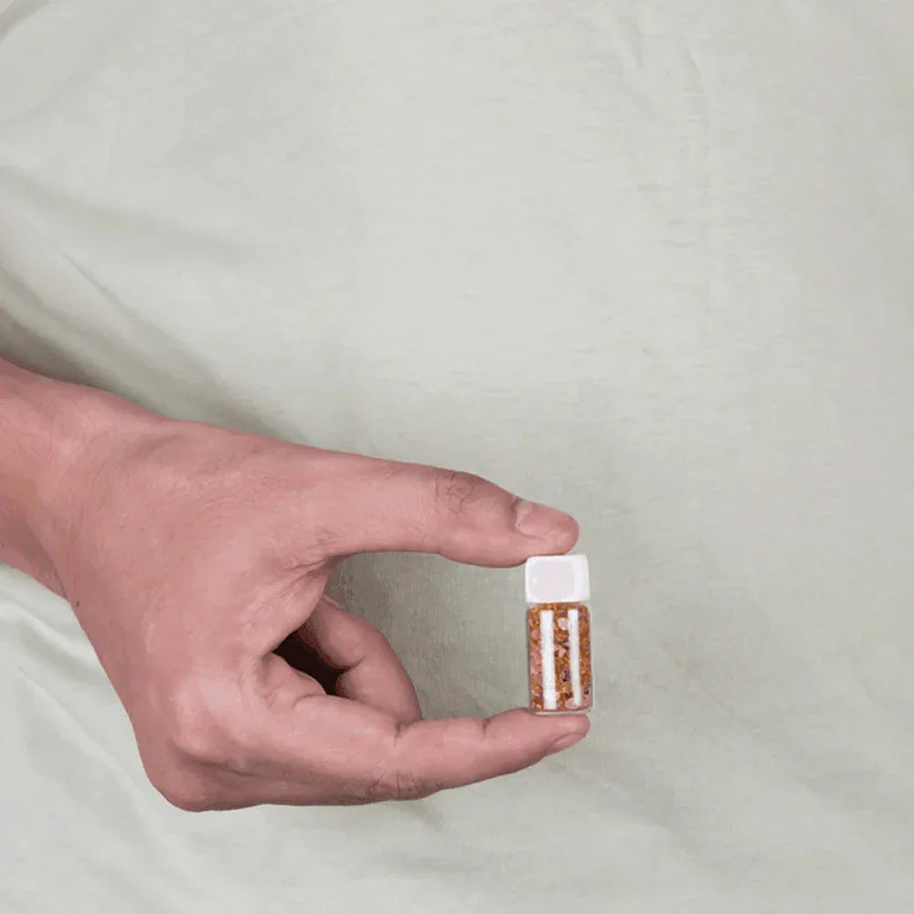 Hand holding a small bottle of MahaVastu Gomed remedy crystals against a light background