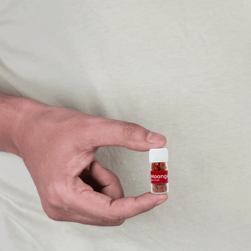 Hand holding a small vial of Moonga coral MahaVastu remedy against a plain background