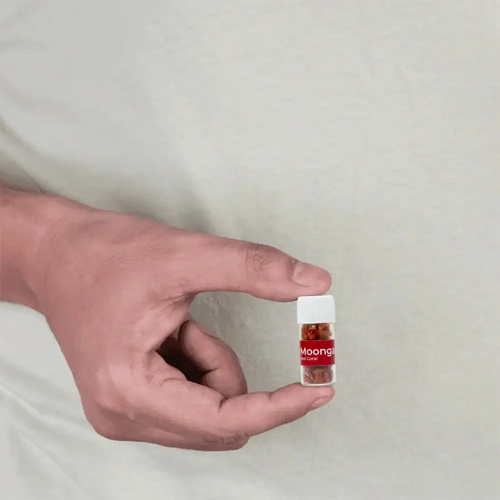 A person holding a small glass vial containing red coral stones for Vastu remedies.