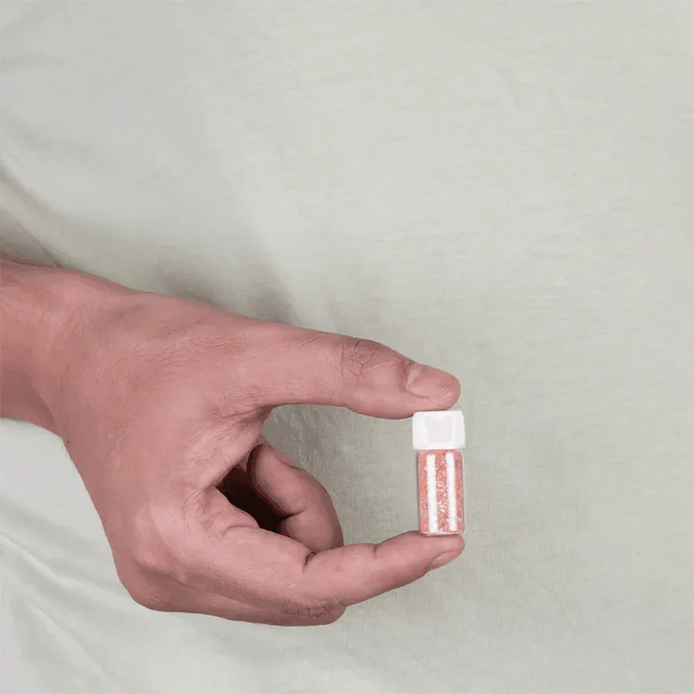 Hand holding a small vial of Moonga coral MahaVastu remedy against a plain background