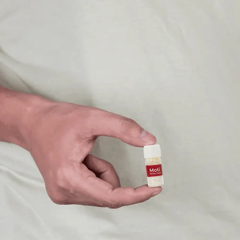 A hand holding a small vial of Moti white pearls for Vastu remedies.
