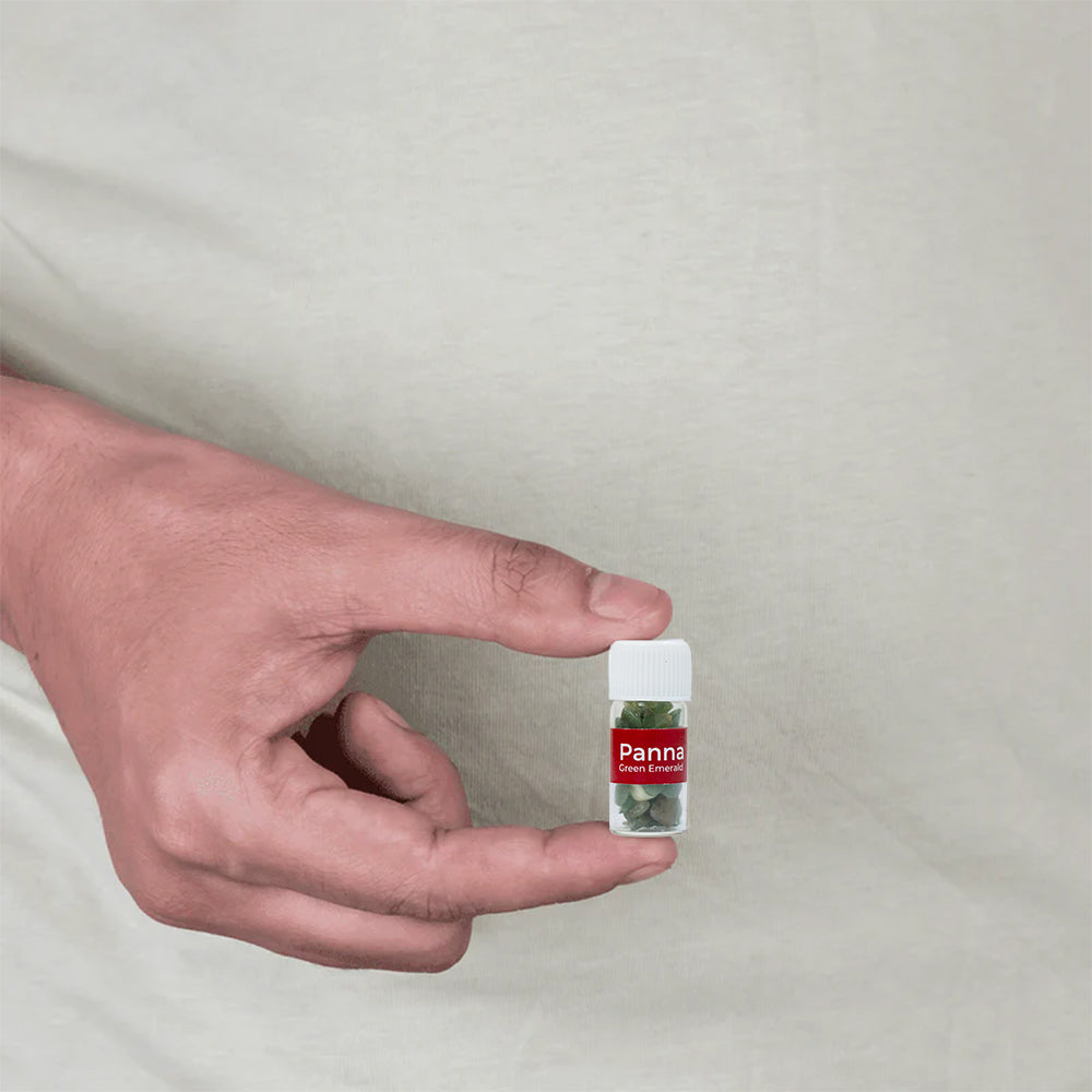 Hand holding a small vial with metal MahaVastu remedy capsules against a plain background