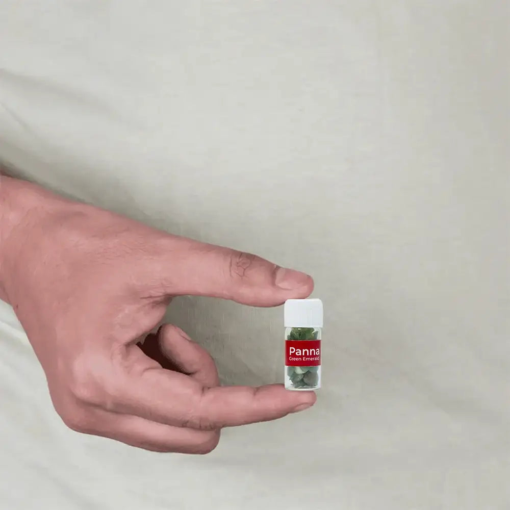 Hand holding small vial of Panna Green Emerald gemstones for Vastu remedies and positive energy