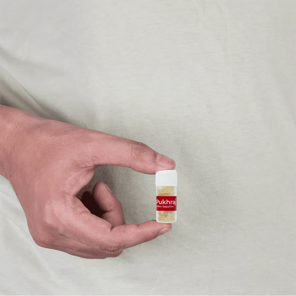 Hand holding a small transparent bottle with yellow Pukhraj stones for MahaVastu remedies
