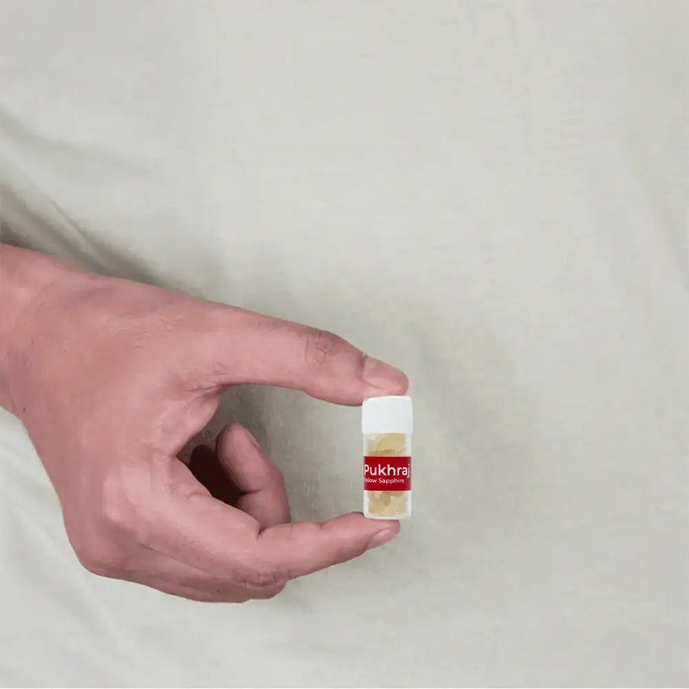 Hand holding small vial of Pukhraj Yellow Sapphire gemstones for Vastu remedies and positive energy