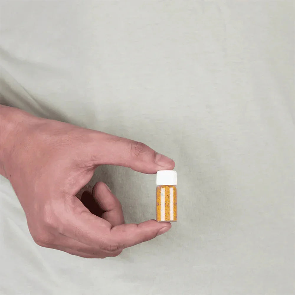 Hand holding a small transparent bottle with yellow Pukhraj stones for MahaVastu remedies