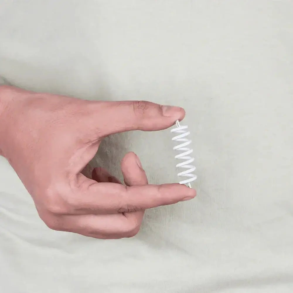 A hand holding a small white spiral metal strip for Vastu remedy application.