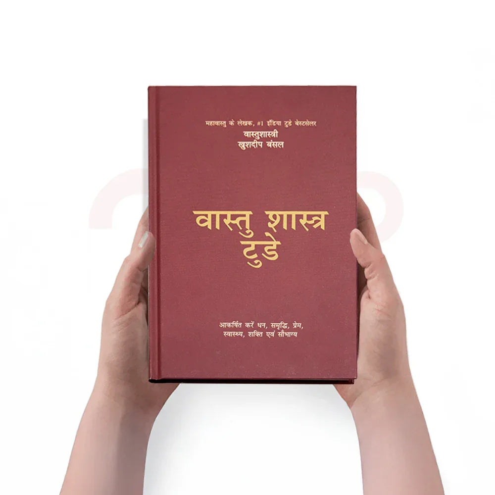 Person holding a Hindi Vastu Shastra remedies book with maroon cover