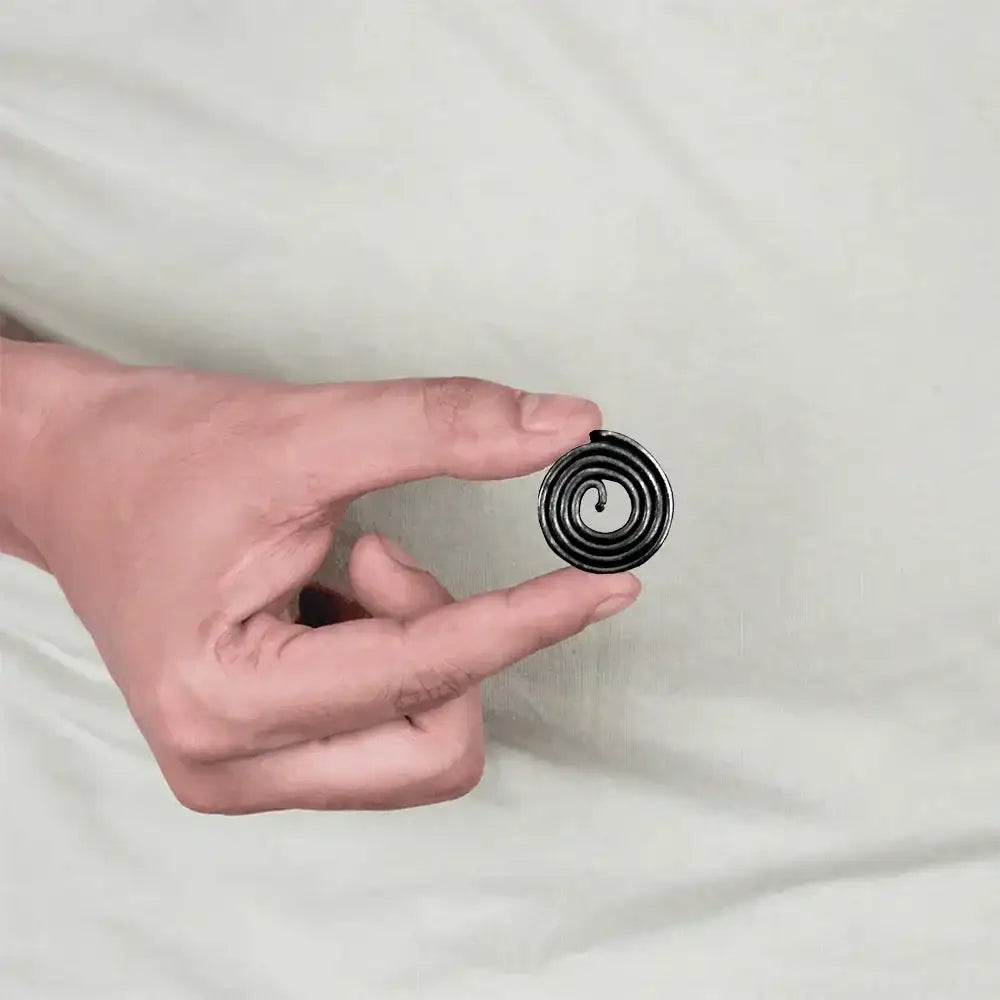 A person holding a small black metal Vastu remedy strip with a spiral design.