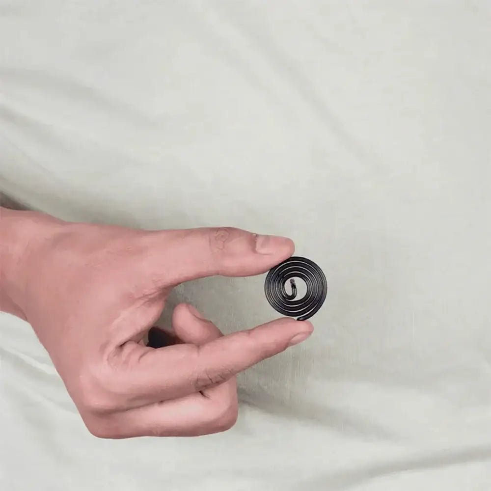 A hand holding a small black metal strip coil for Vastu Shastra remedies.